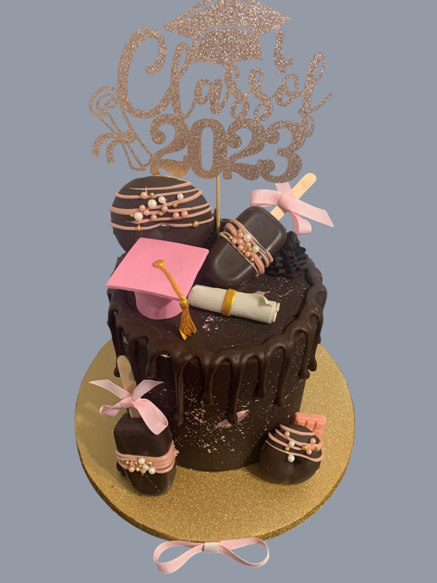Sarah's Cakes chocolate graduation cake with 'Class of 2023' topper, pink graduation cap, diploma, and cake pops.