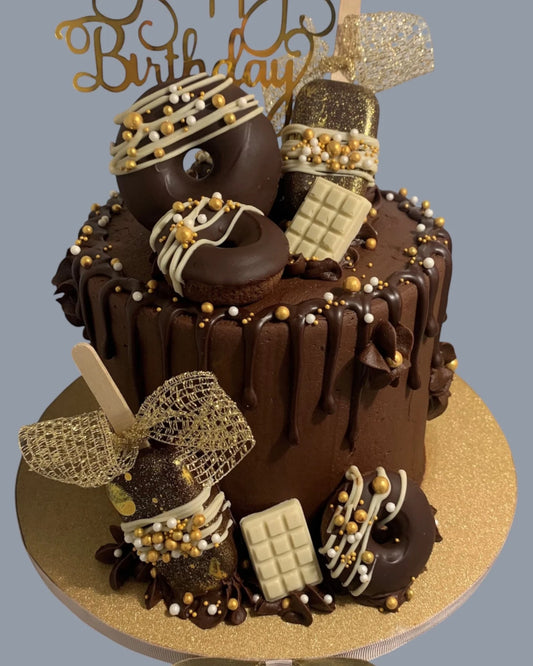 Sarah's Cakes chocolate drip cake with donuts, chocolate bars, and gold sprinkles, topped with a 'Happy Birthday' topper.
