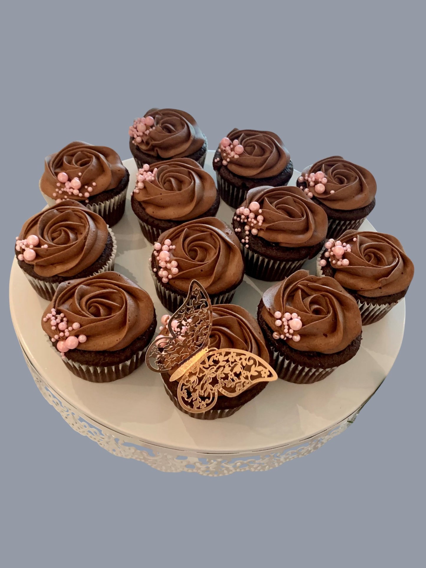 Sarah's Cakes chocolate cupcakes with chocolate frosting, topped with pink pearls and a gold butterfly decoration.