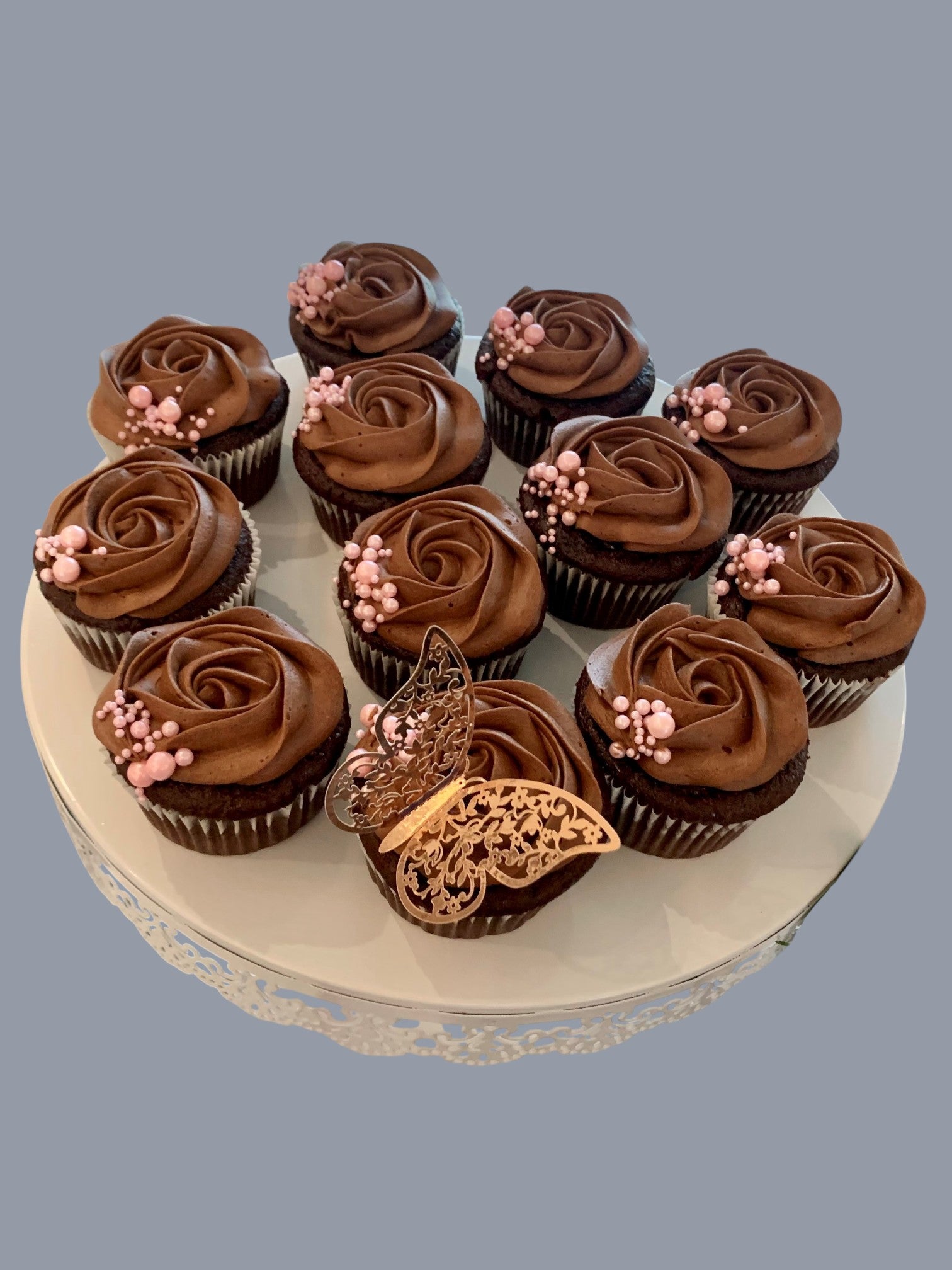 Sarah's Cakes chocolate cupcakes with chocolate frosting, topped with pink pearls and a gold butterfly decoration.