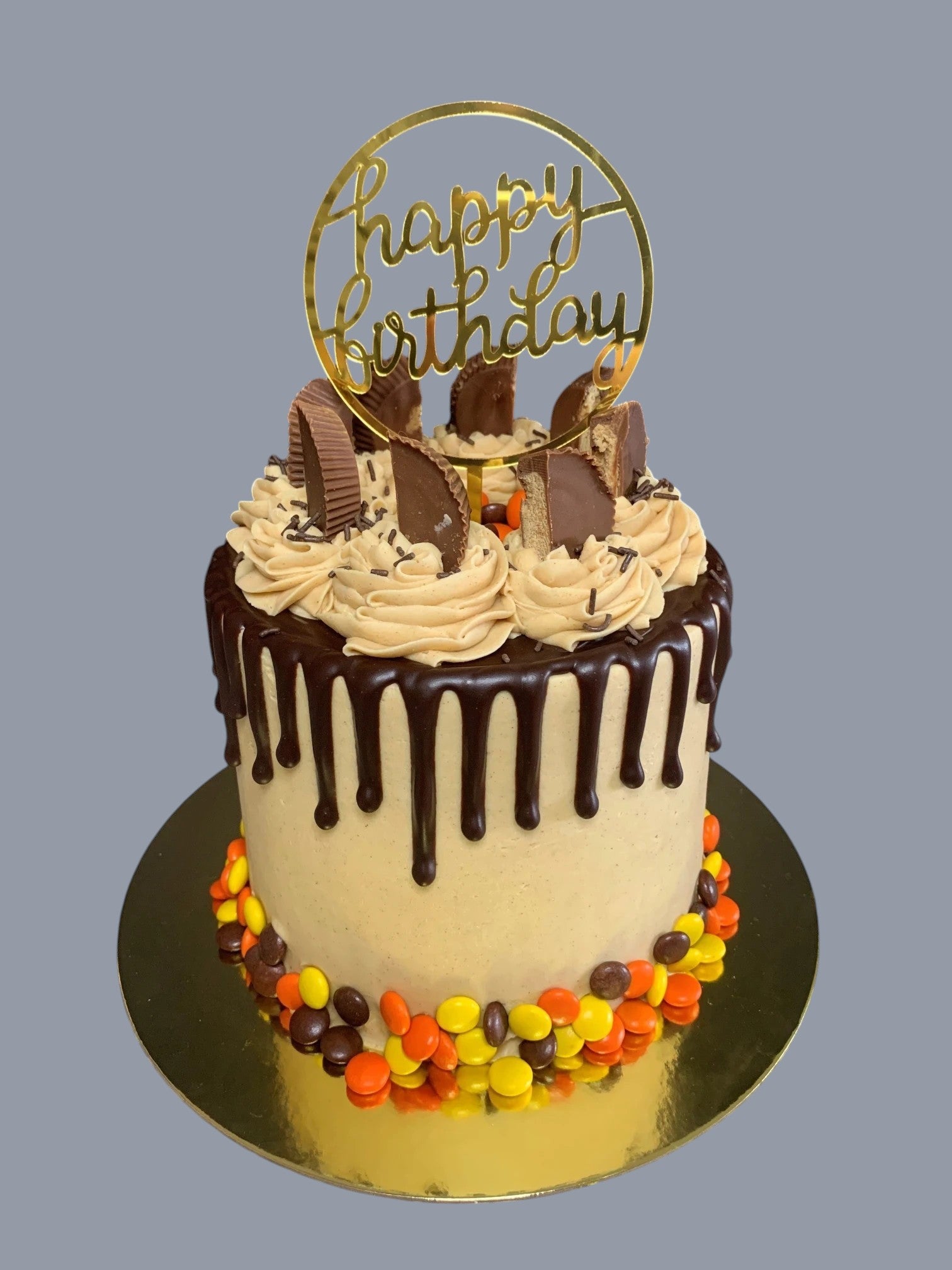 Sarah's Cakes peanut butter drip cake with chocolate ganache, Reese's peanut butter cups, and a gold 'happy birthday' topper.