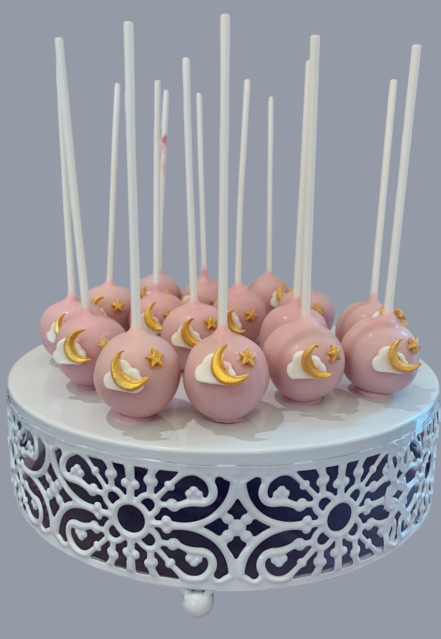 Sarah's Cakes pink cake pops decorated with gold moons, clouds, and stars on white cake stand.