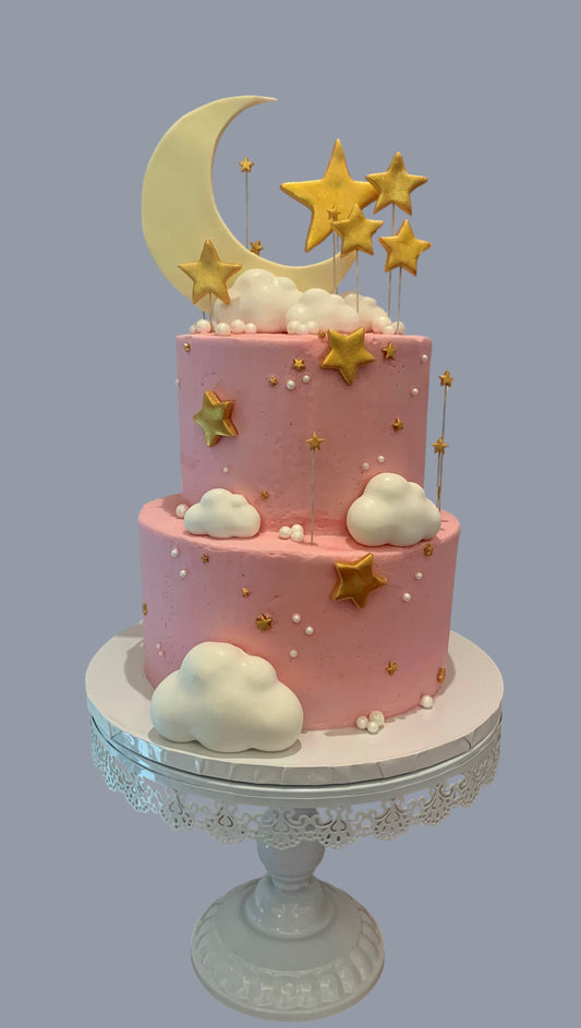Sarah's Cakes two-tier pink sculpted cake with white fondant clouds and gold stars, topped with a large crescent moon.