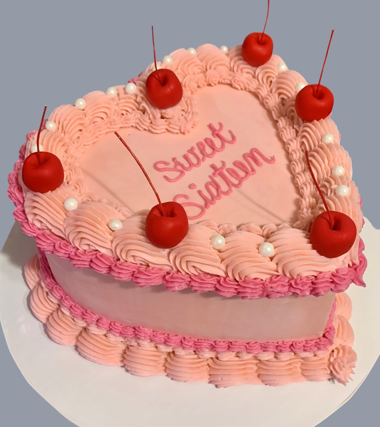 Sarah's Cakes vintage heart cake with pink frosting, piped details, white pearls, and maraschino cherries. "Sweet Sixteen" written in pink script.